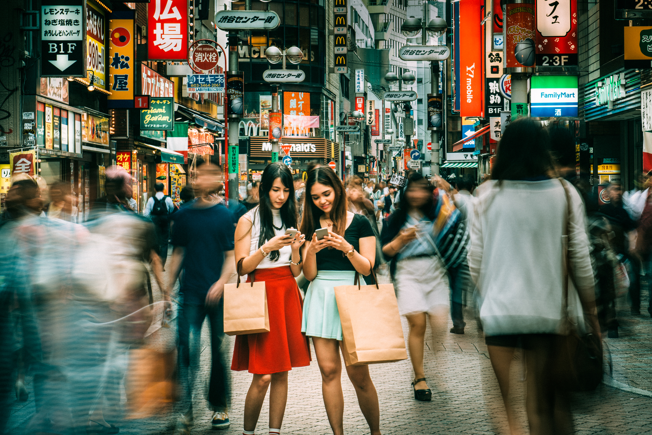 2 women on Tokyo street looking at their mobile phones