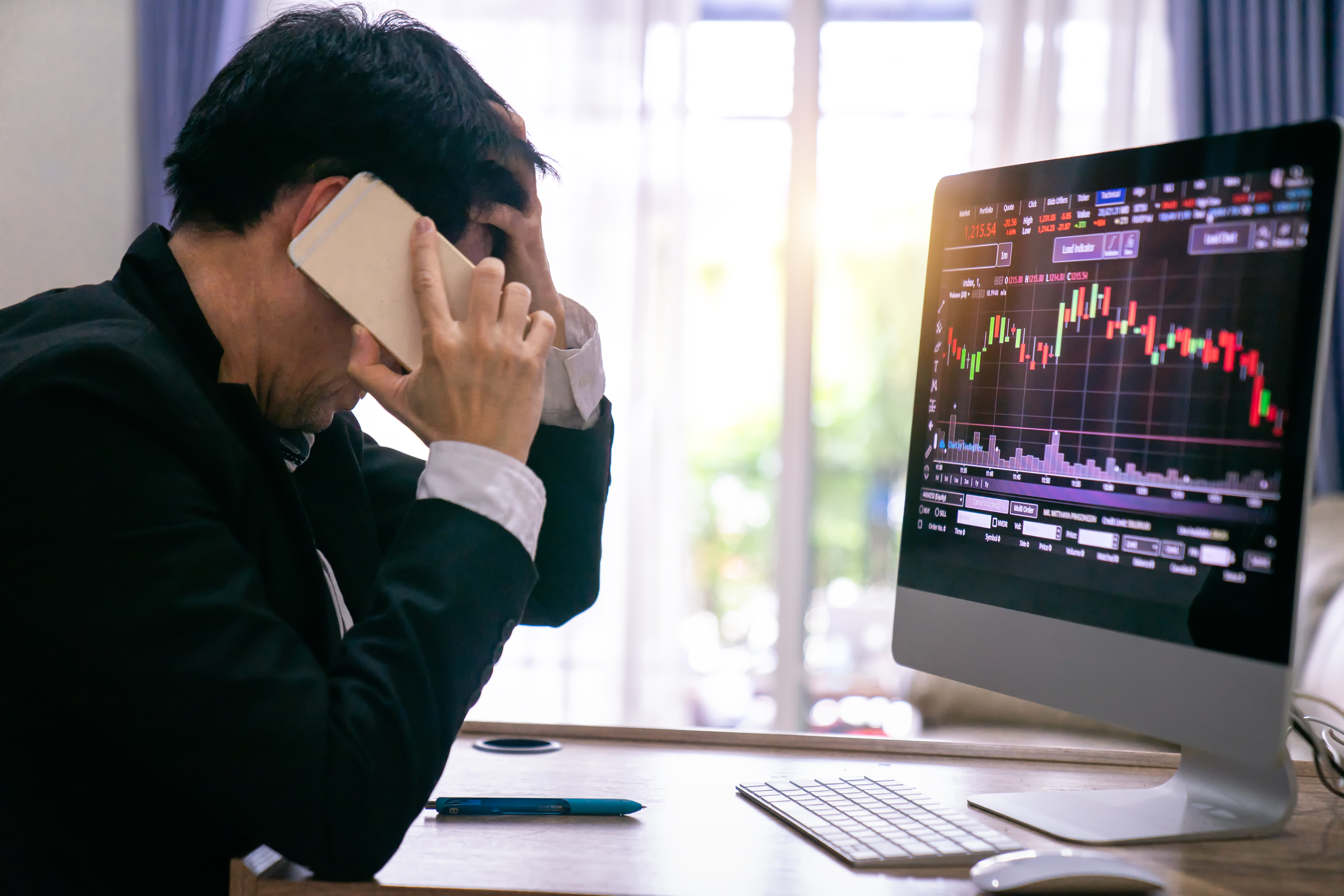 Image of a stressed businessman looking at screen of falling stocks.