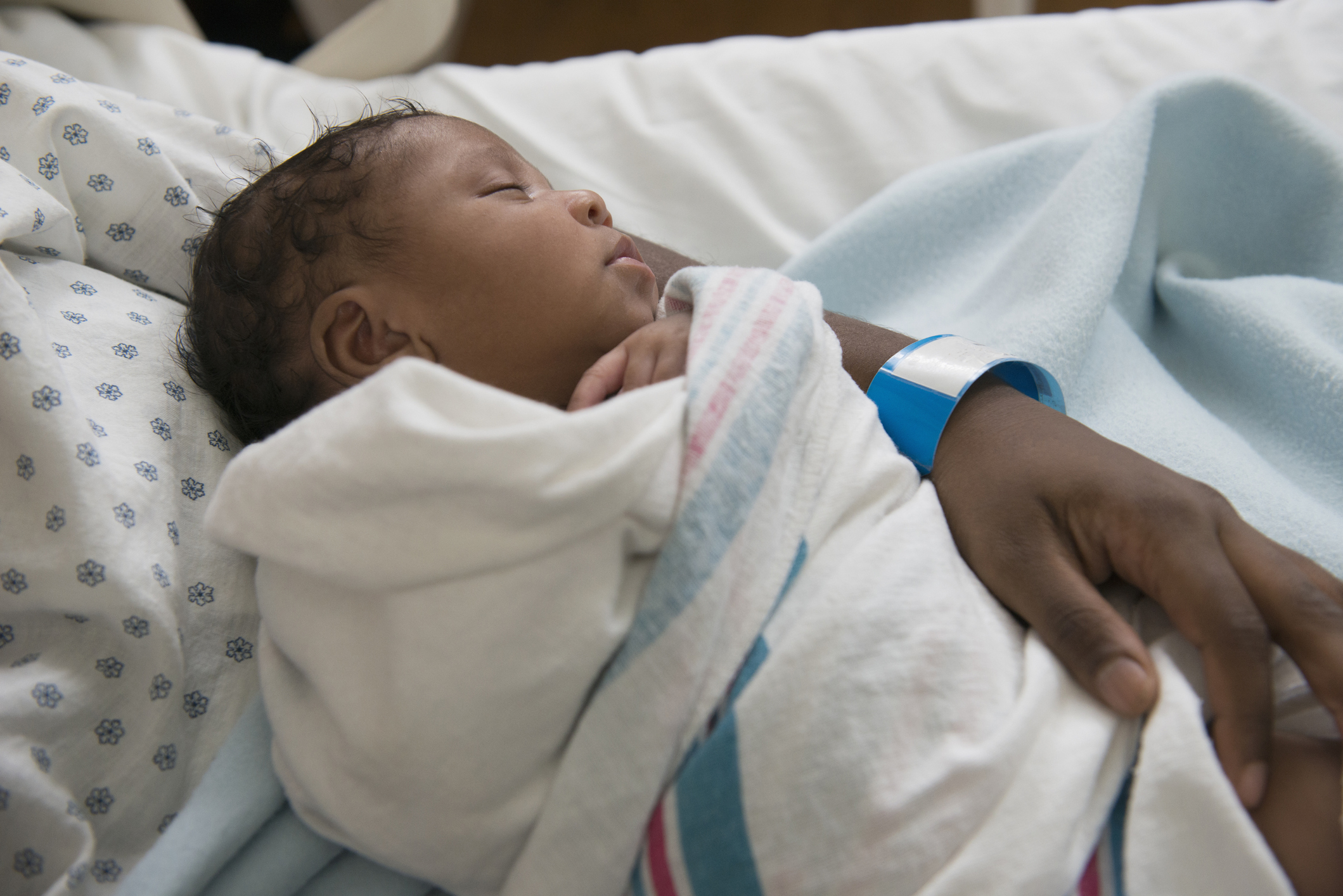 Newborn Black child in her mother's arms at the hospital, swaddled in a blanket.