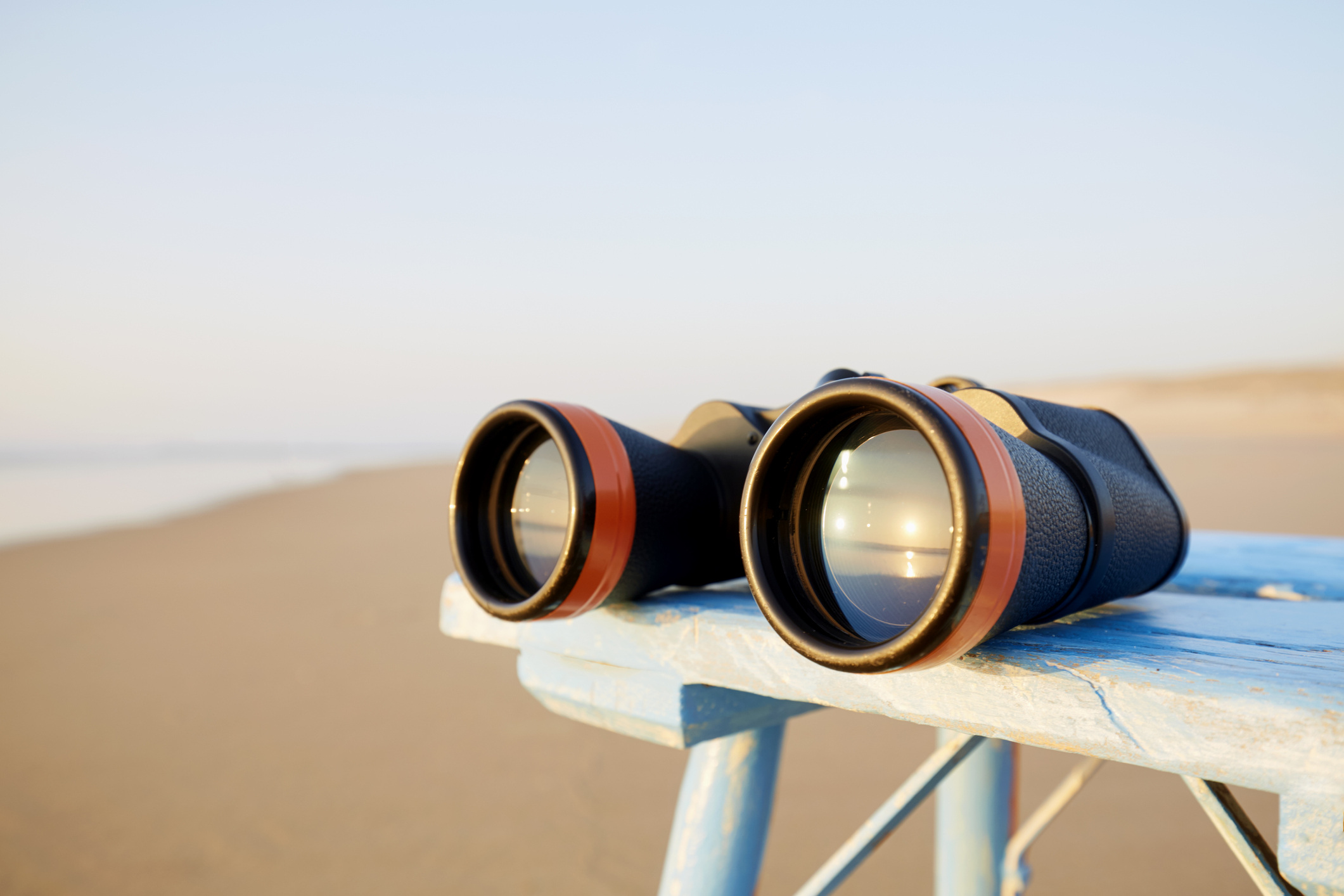 Close-up of binoculars on table by the sea during sunset, the sunset is reflected in the glass of the binoculars