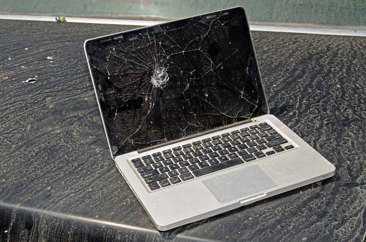 Broken, dirty and abandoned laptop with cracked screen. Laptop looks like it has been left outdoors in the elements for quite some time.