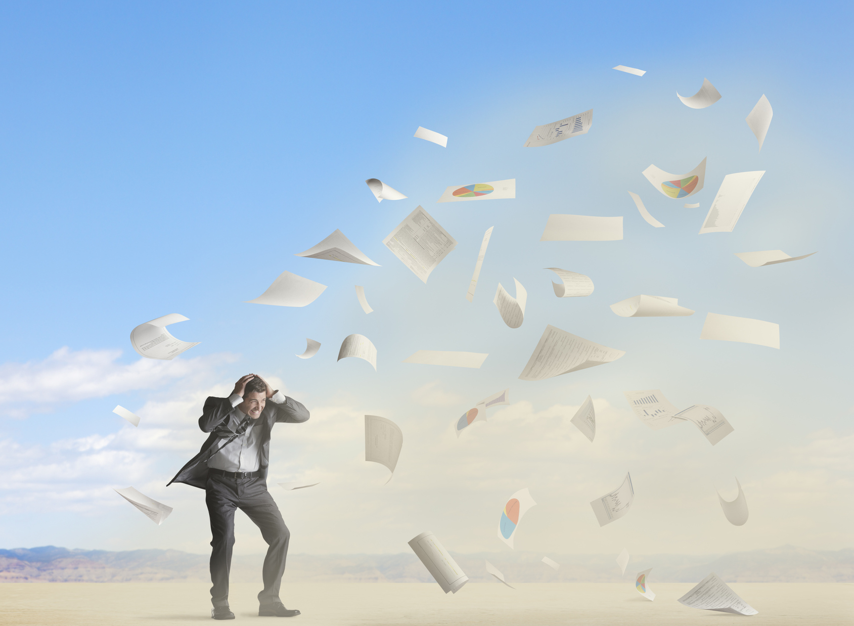A business man caught in a whirlwind of paperwork and graphs.