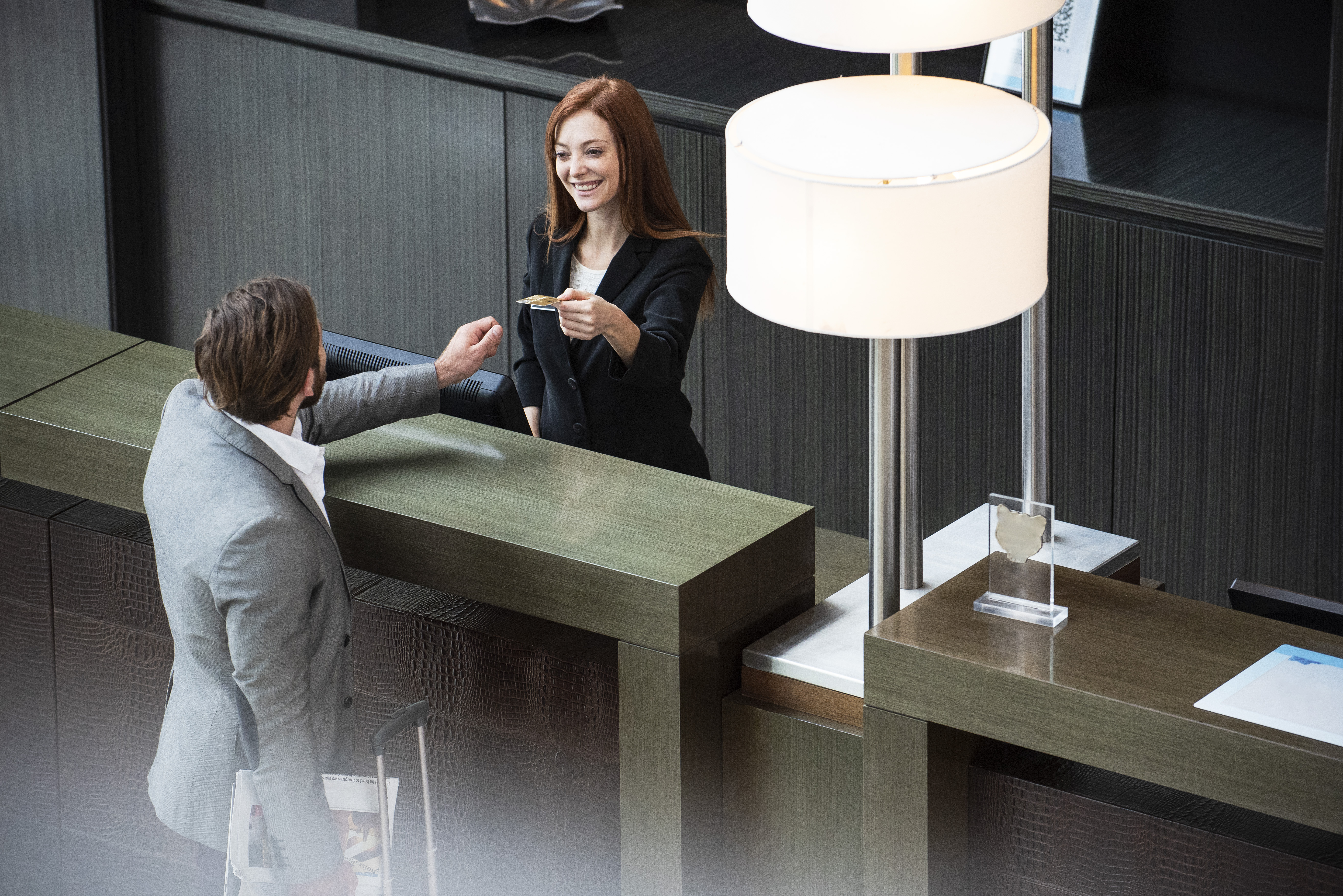 Smiling female receptionist giving credit card to businessman while standing at hotel reception