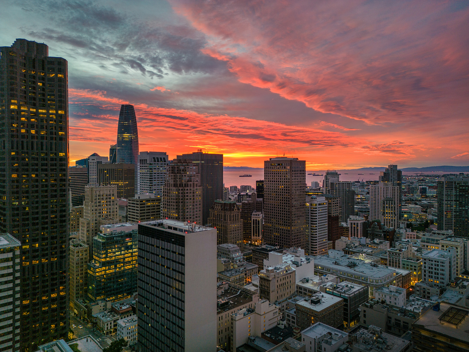 Aerial view over San Francisco with a burning sunrise over the Bay. Skyscrapers fill the skyline.