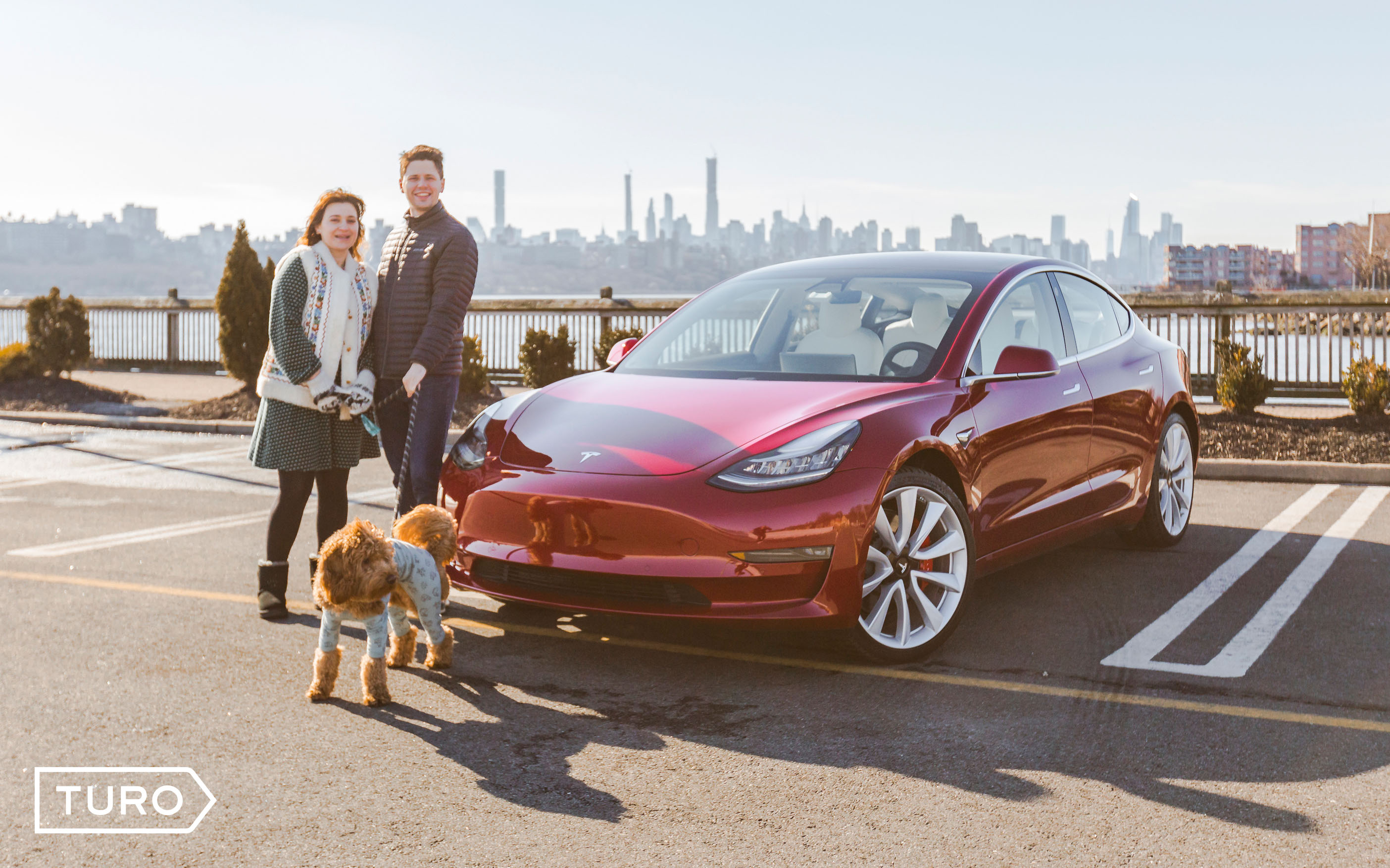 man woman and dog standing in front of red tesla in a parking lot