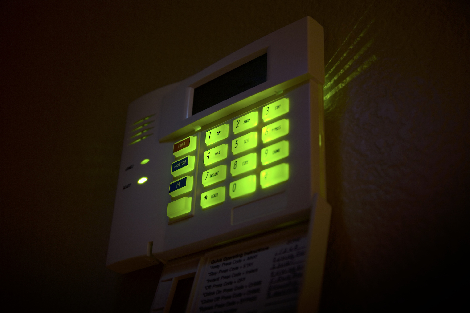 a security alarm keypad lit up with green buttons in a darkened room