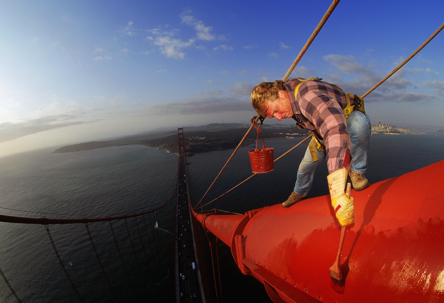 A worker standing on a suspension cable of the Golden Gate Bridge applies a new coat of paint