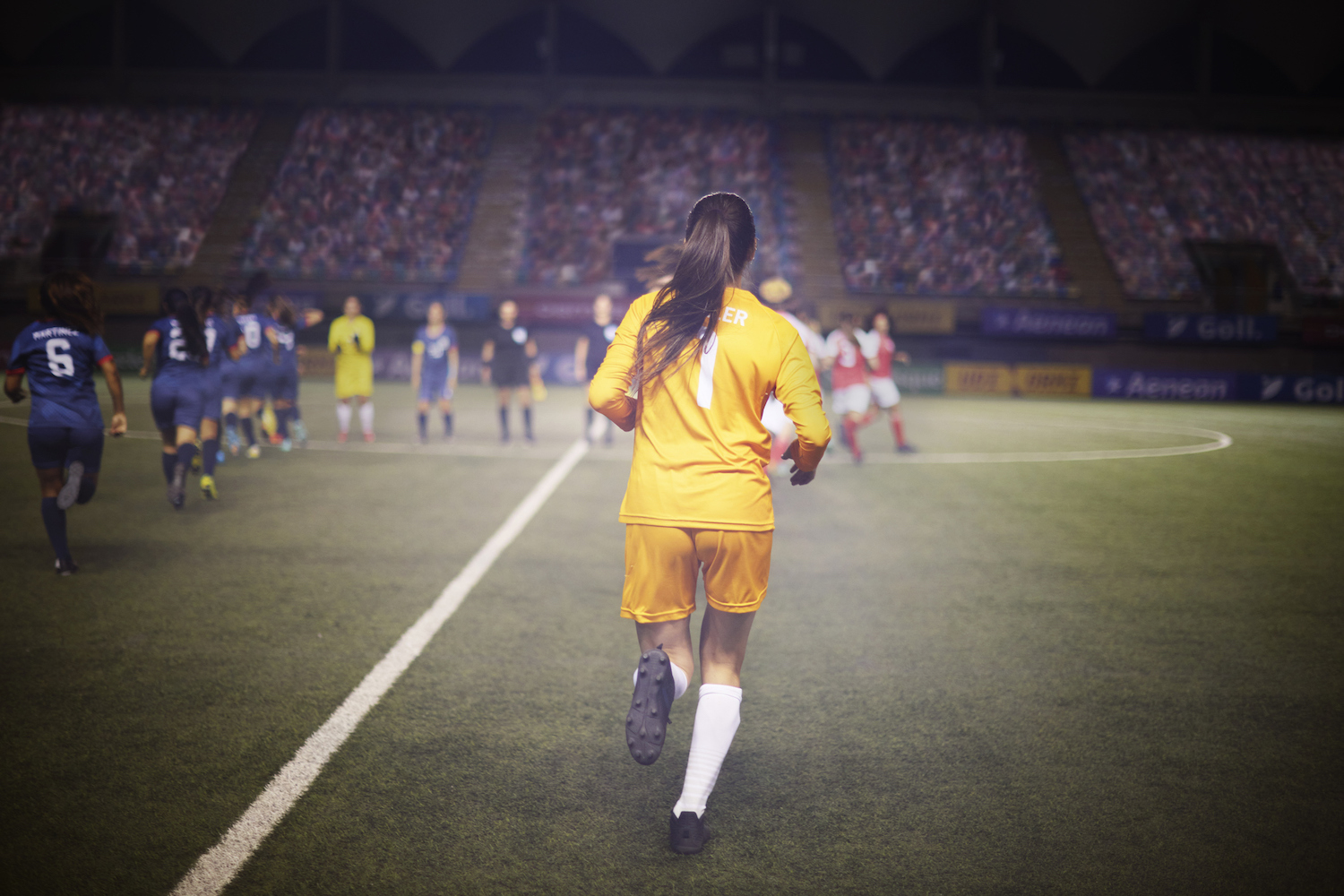 Determined female goalie jogs onto the field with her soccer teammates and alongside the opposing team for the pregame ceremony