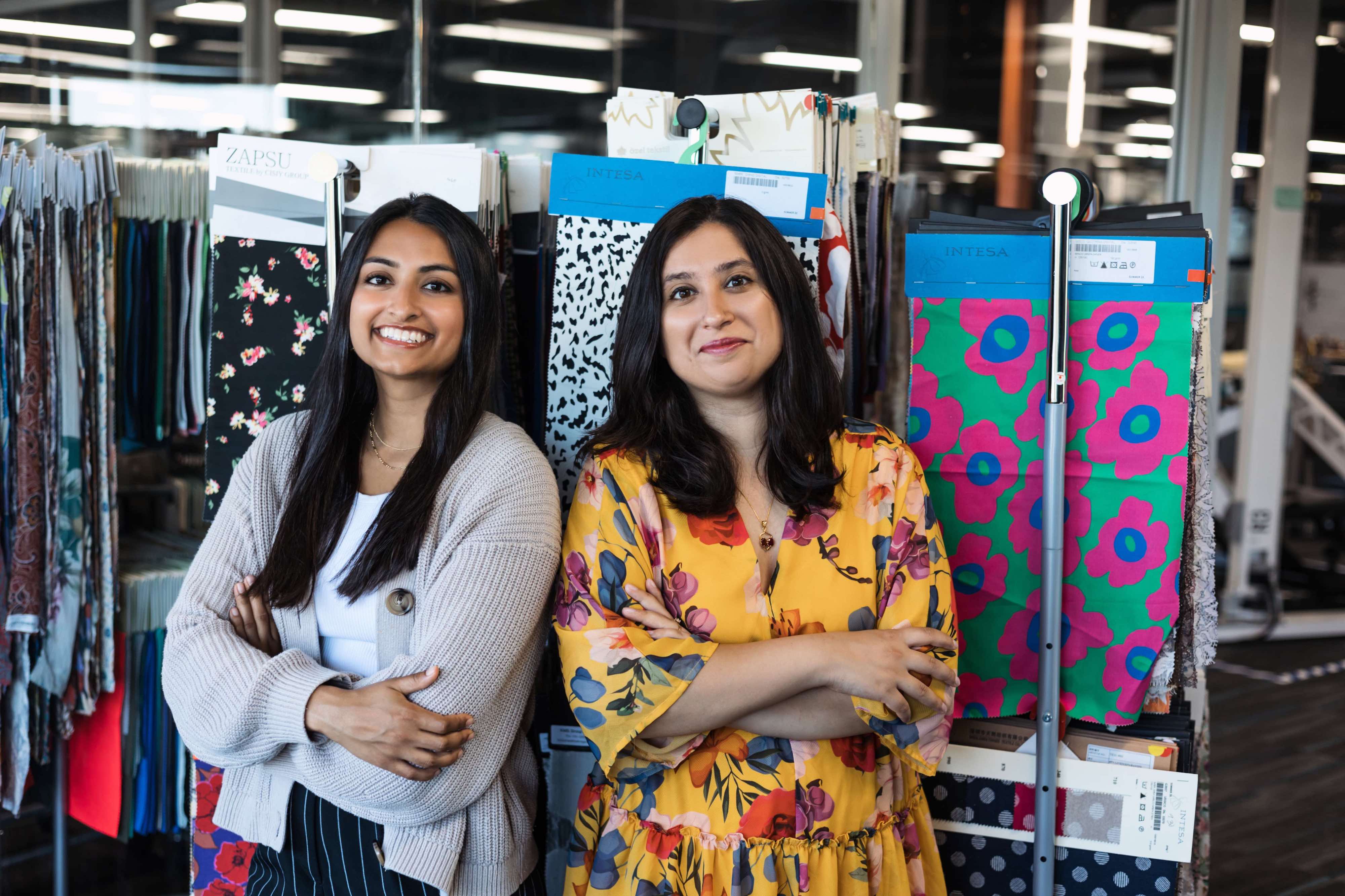 Refiberd founders Tushita Gupta and Sarika Bajaj stand before colorful textile samples.
