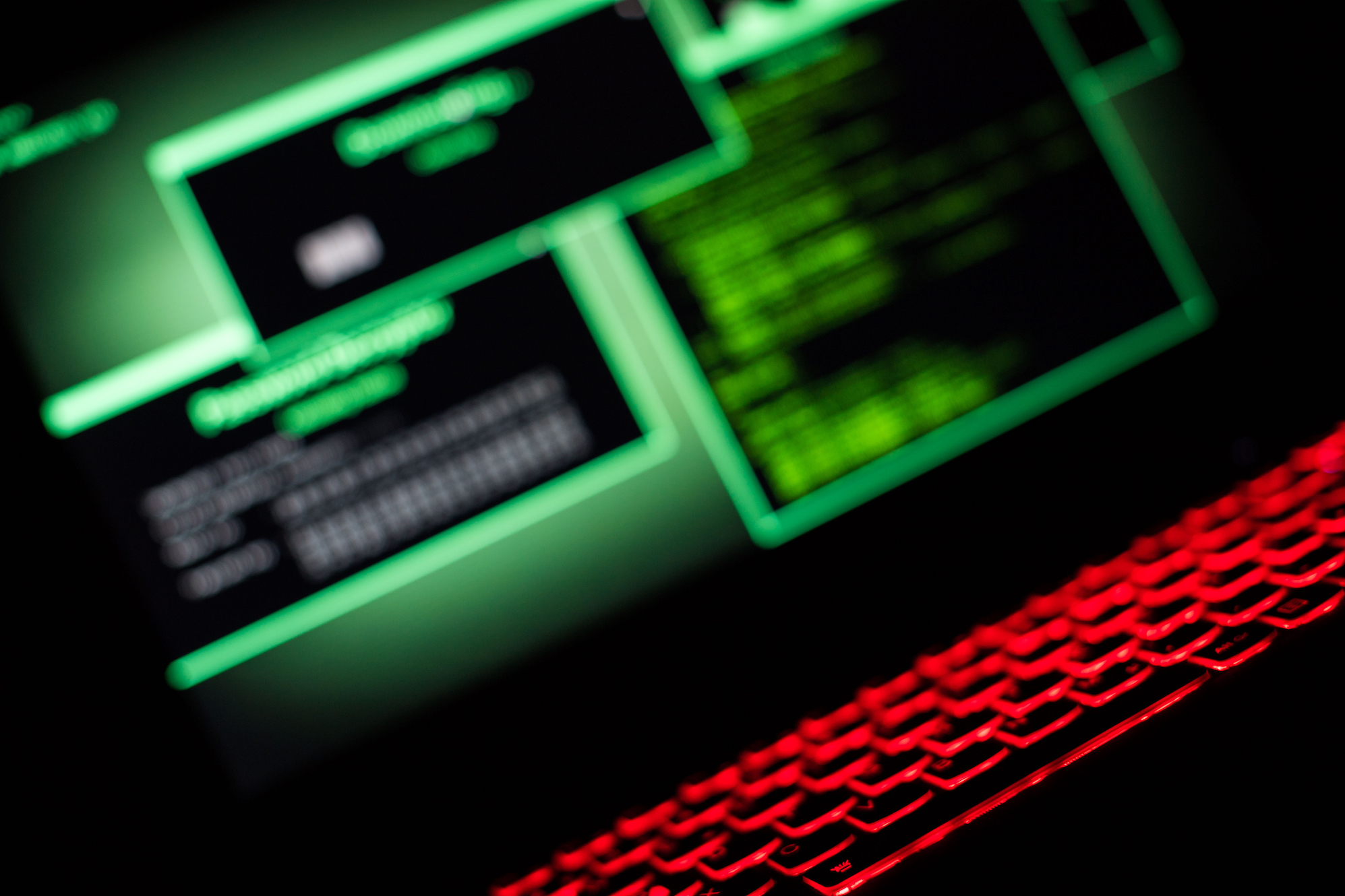 a photo of an angled computer in a dark room, featuring green windows on a computer display and a red glowing keyboard.