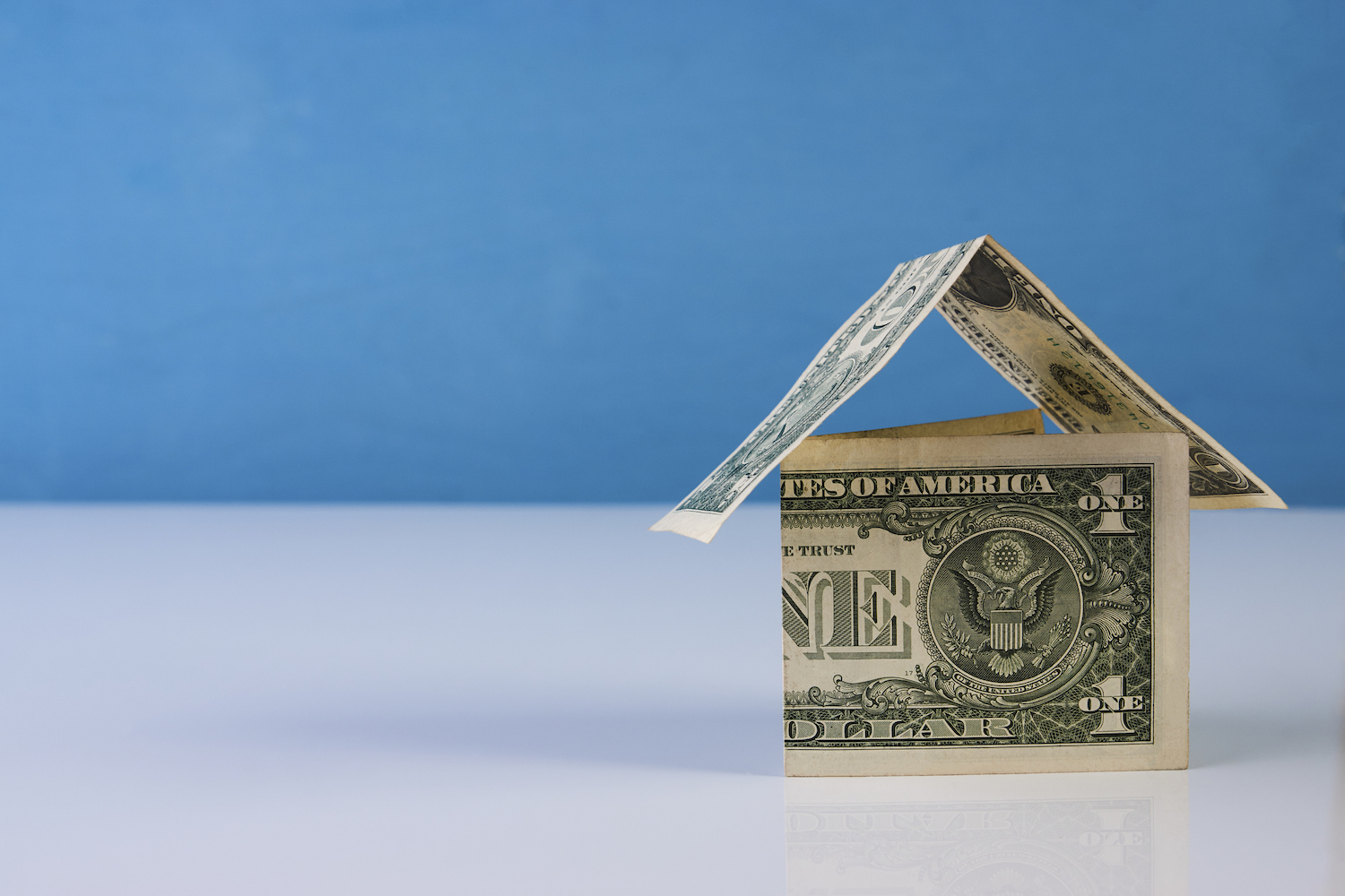 Home made from dollar notes on blue and white background, close-up. Mortgage concept