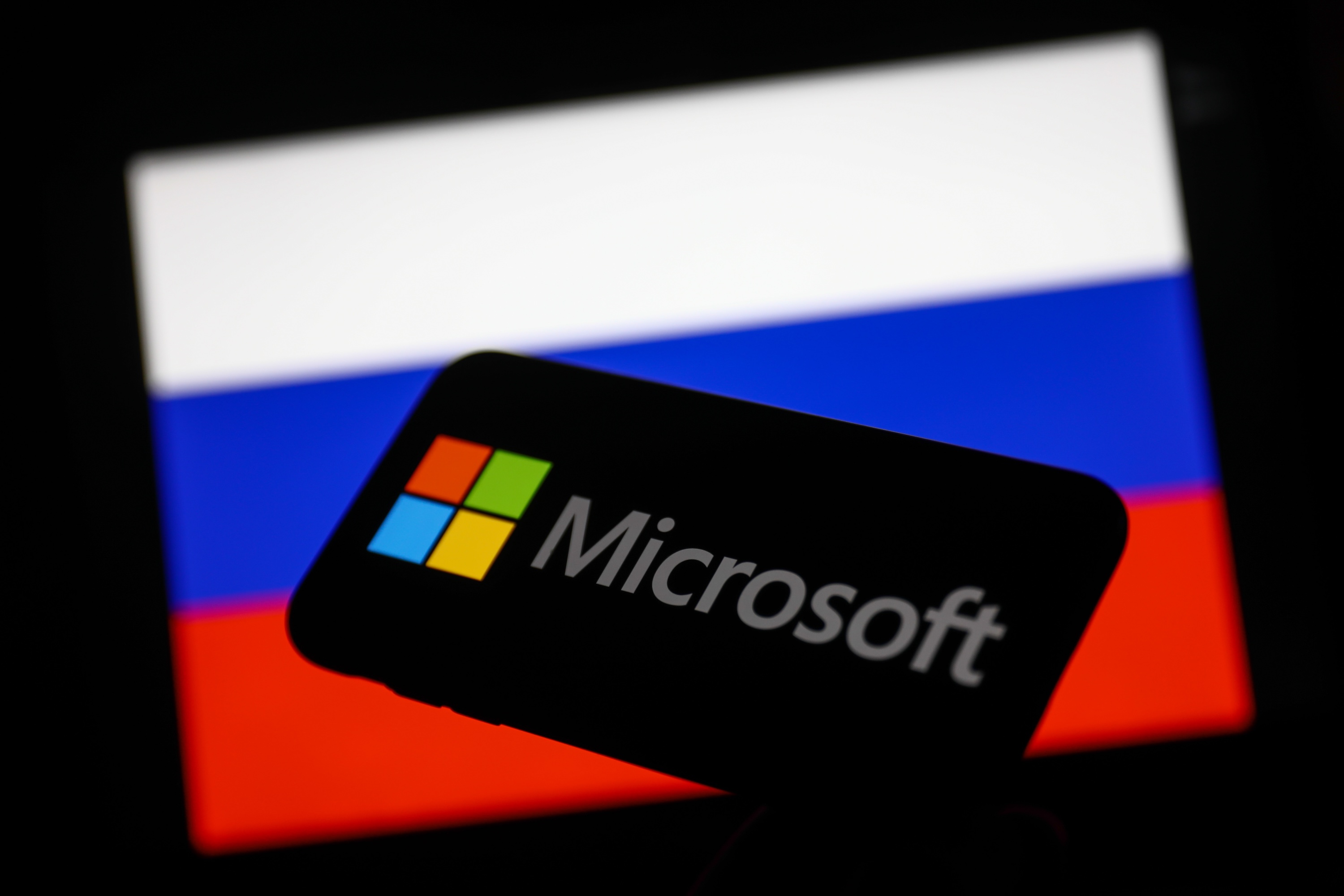 Microsoft logo displayed on a phone screen and Russian flag displayed on a screen in the background.