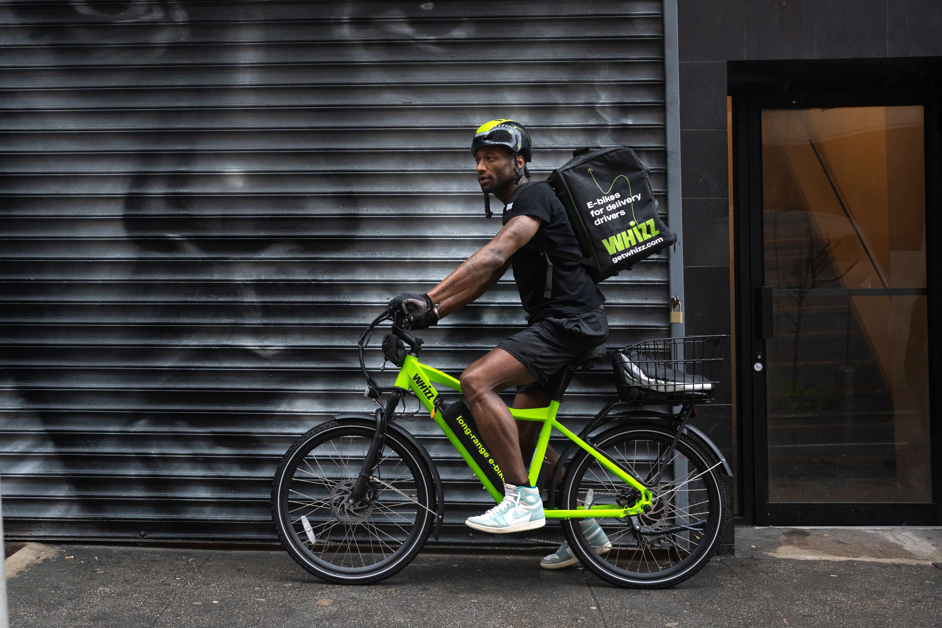 Side shot of food delivery worker on Whizz e-bike on NYC street in front of street mural