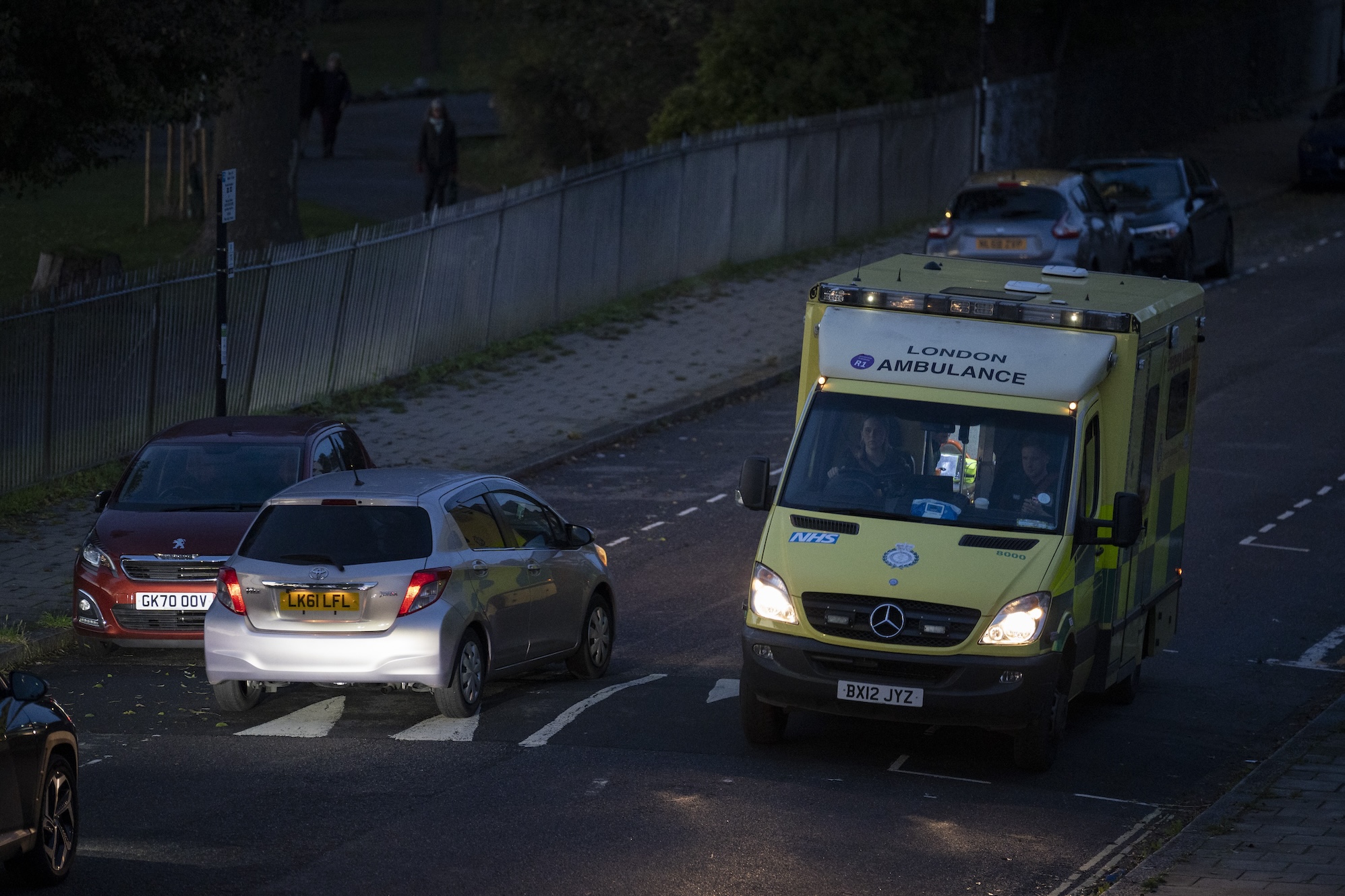 Seen from a high perspective, a London Ambulance passes an oncoming car at dusk on a residential street in Lambeth, south London, on 27th October 2023