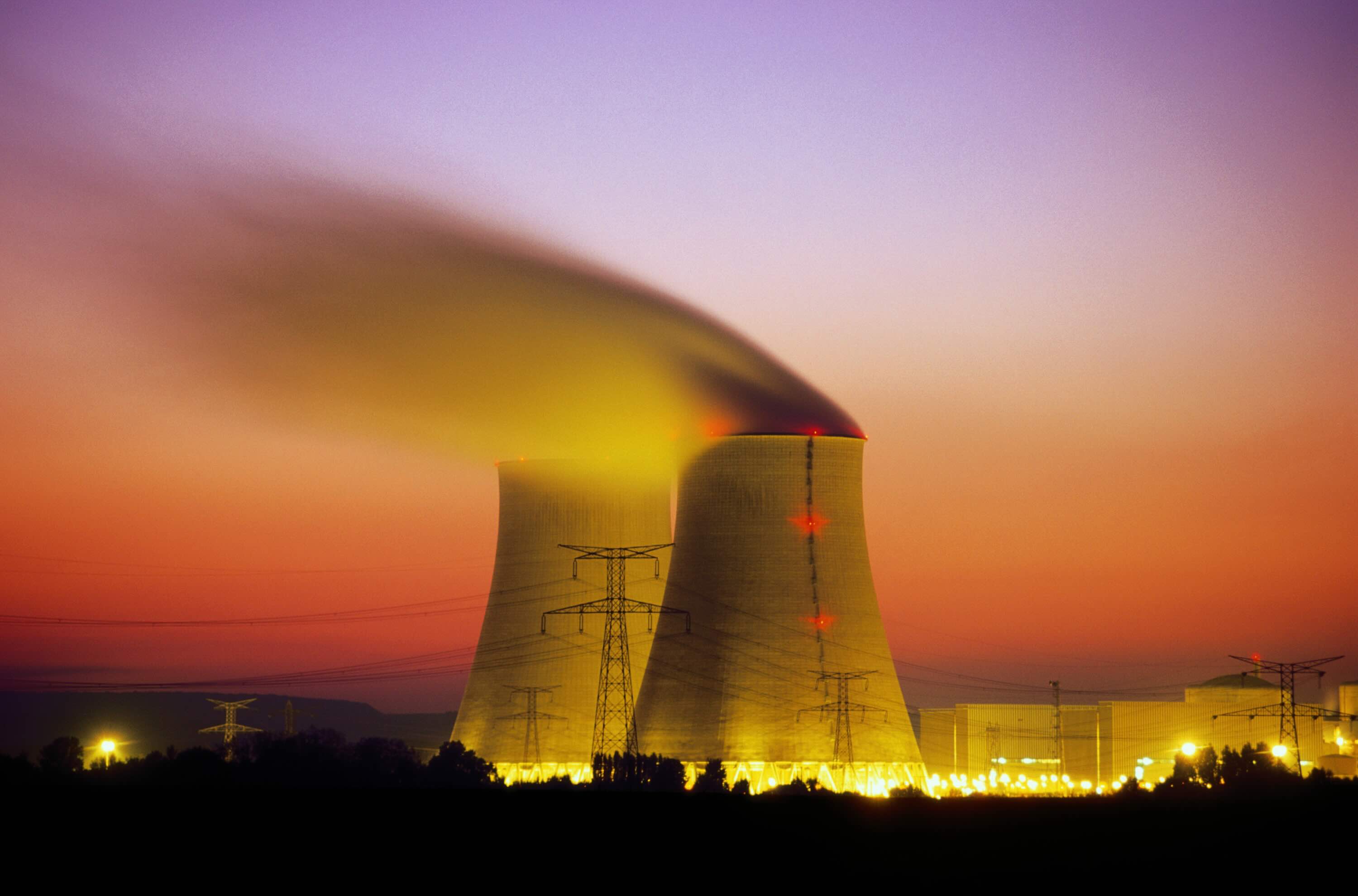 Nuclear power plant cooling towers emit steam at dusk.