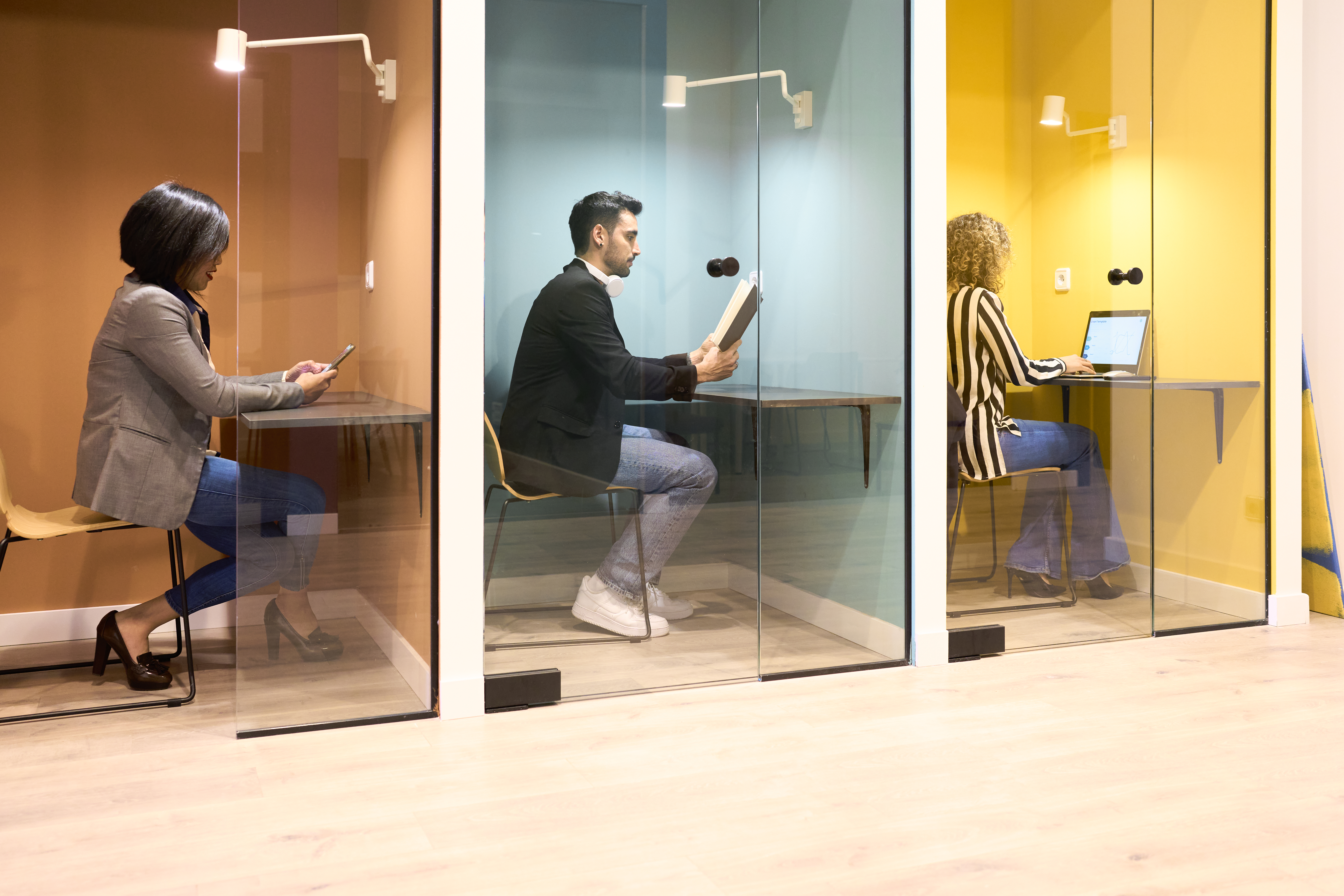 Train coworkers each sitting at the desk in their office cabin with a glass door, working