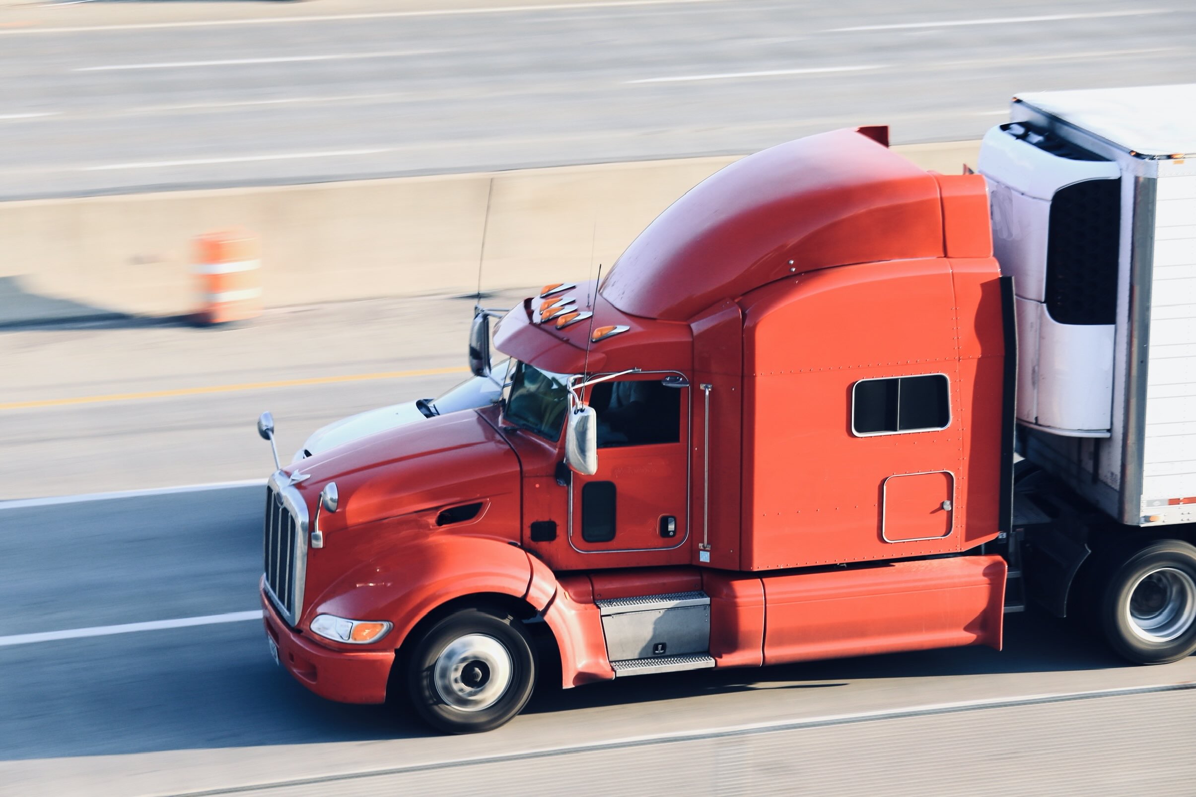 A red semi towing a trailer drives down a highway.