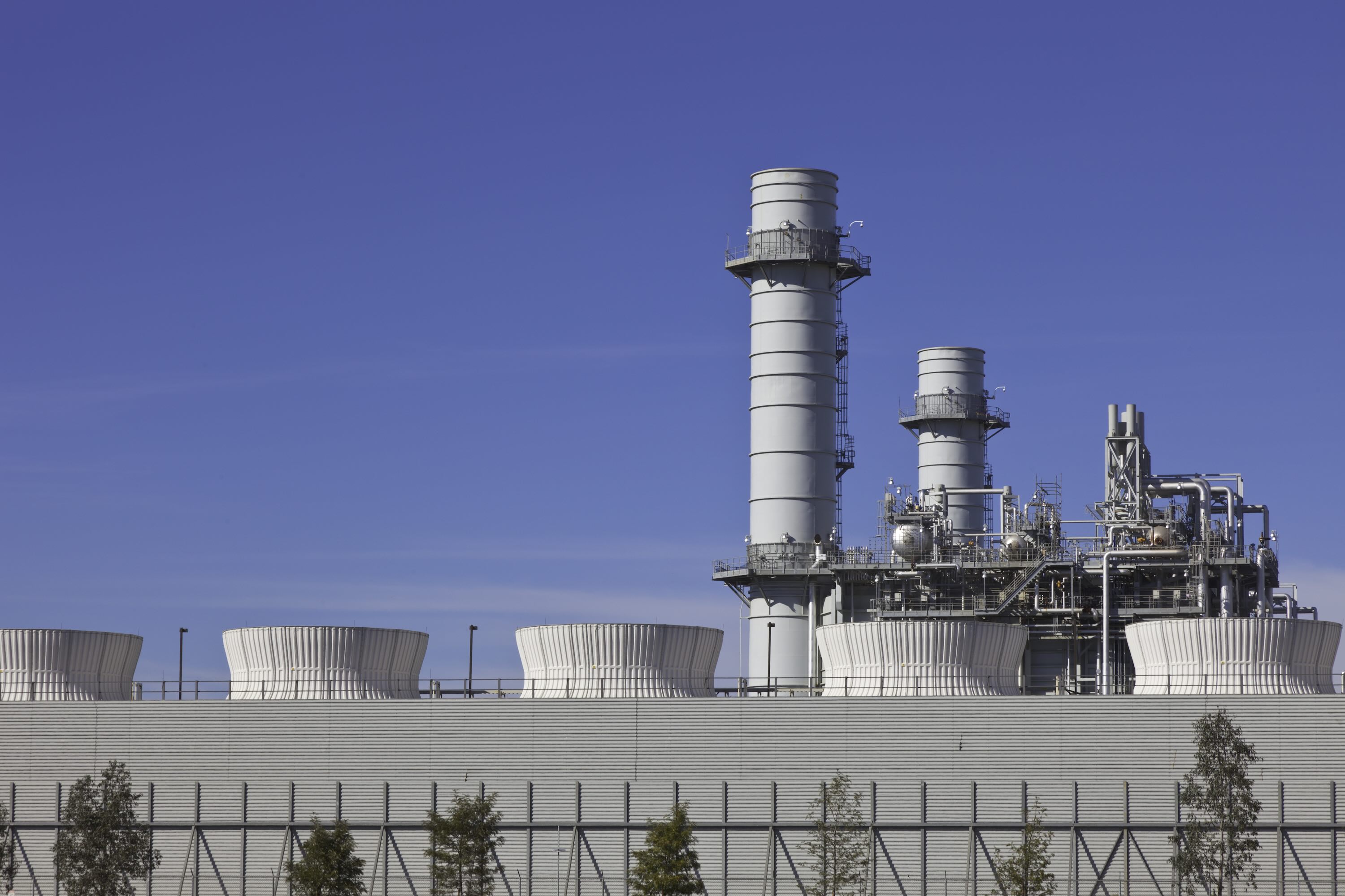 Smoke stacks from a natural gas power plant stand against a blue sky.