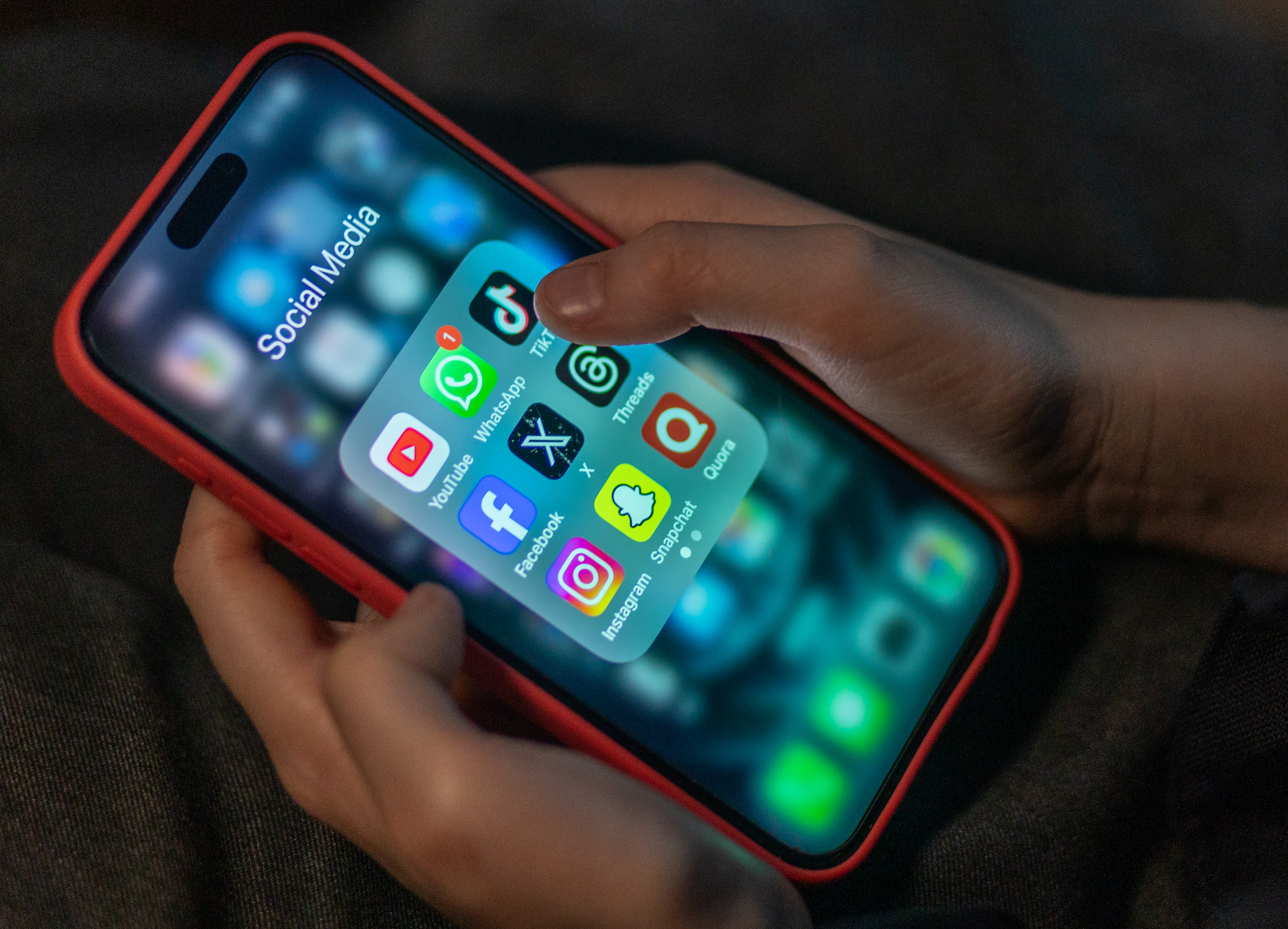A 12-year-old boy looks at an iPhone screen showing various social media apps.