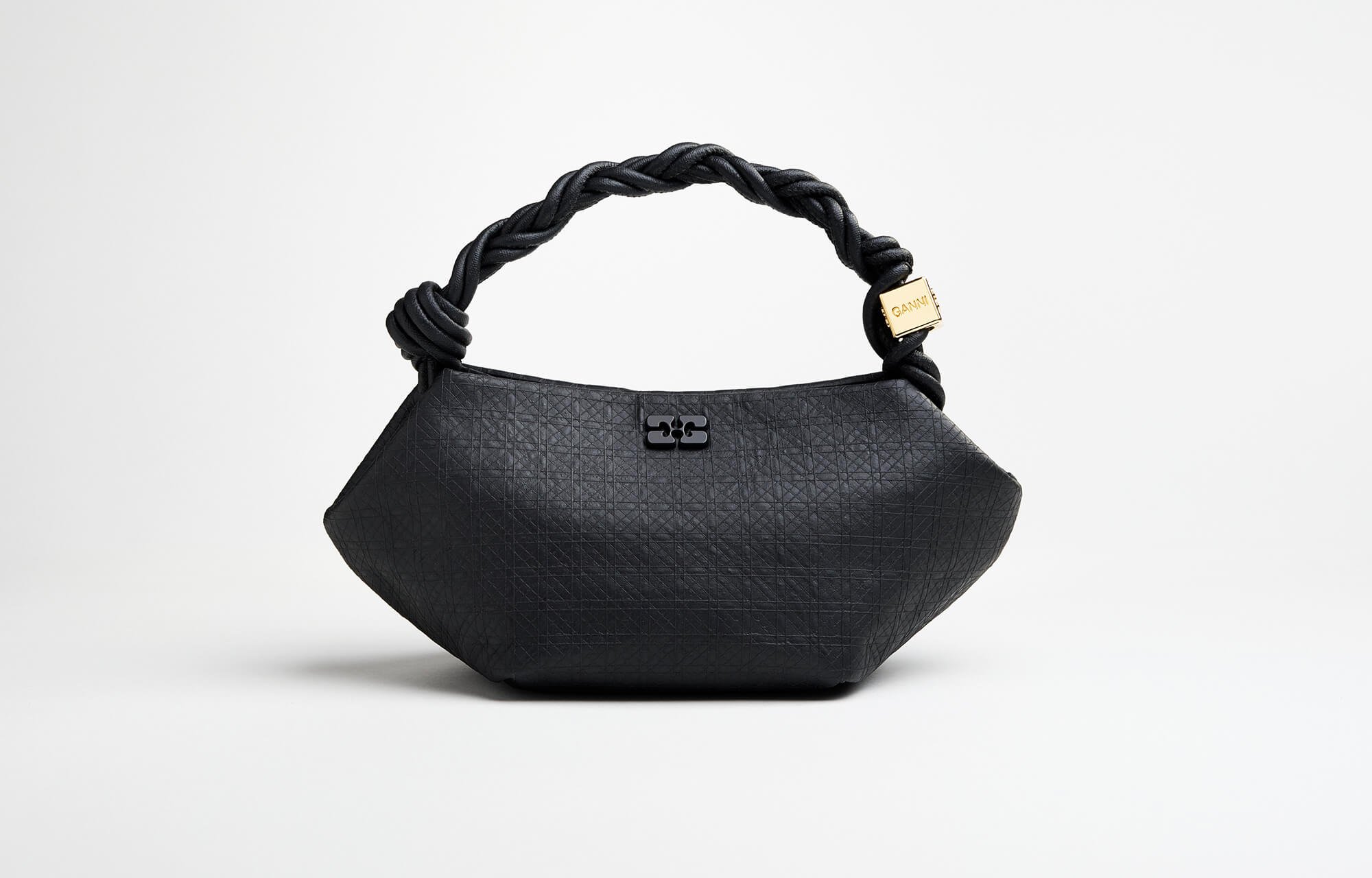 A black handbag sits in front of a white backdrop.