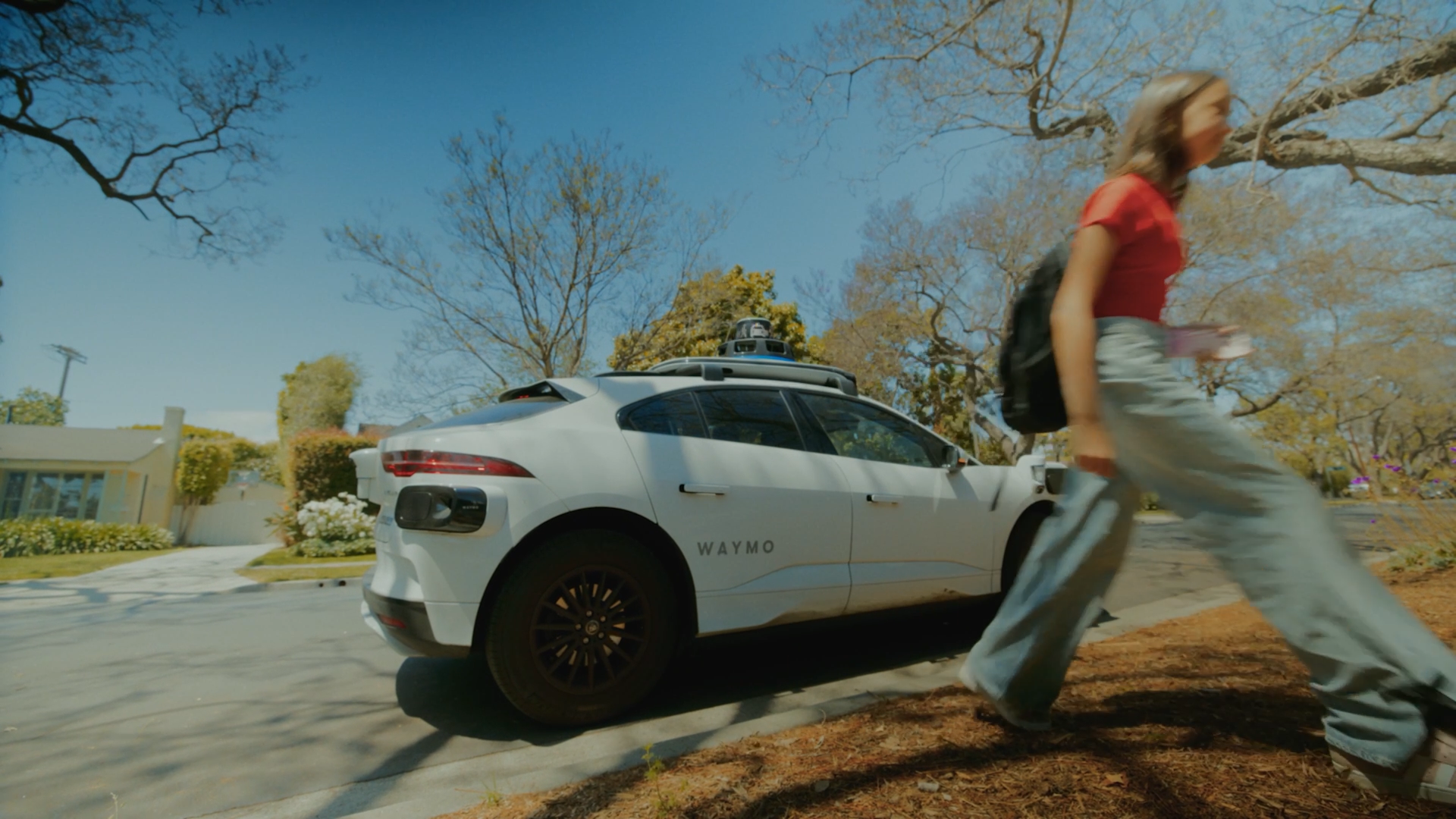 A Waymo robotaxi on the street in Phoenix and a teenage girl walking away from it.