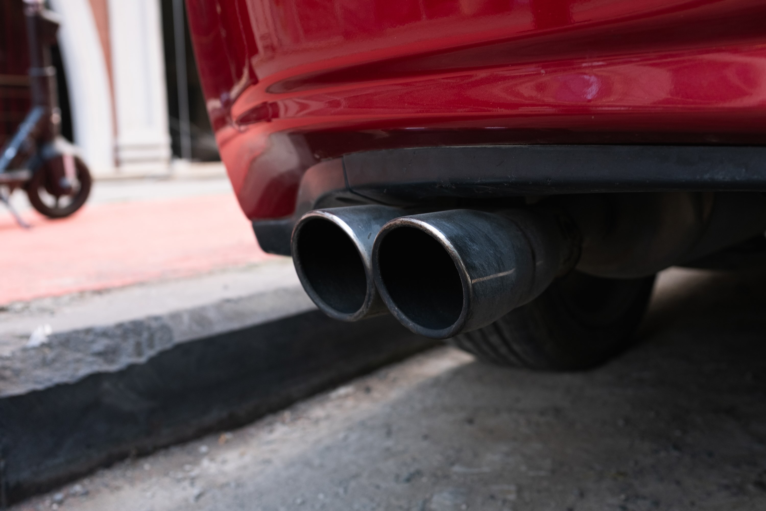 A car parked at a curb viewed with a close-up on the exhaust pipe.