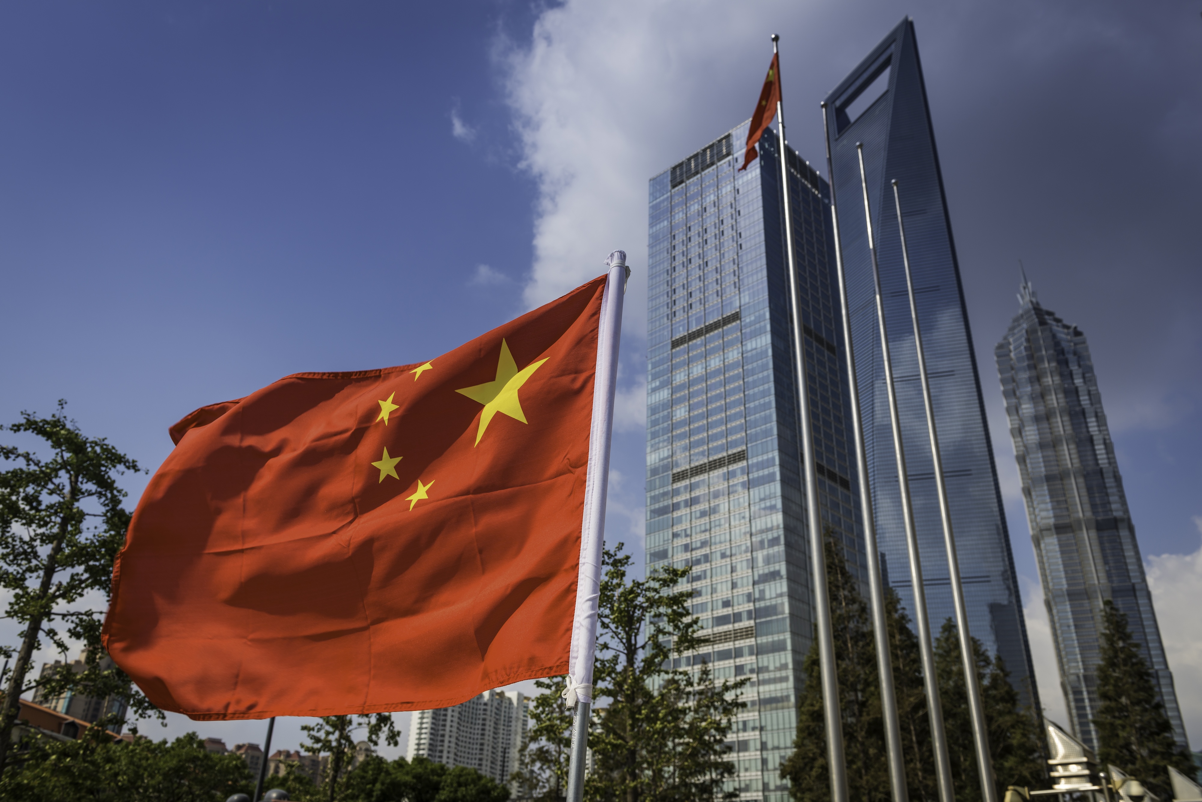 The vibrant red field and yellow stars of the Flag of the People's Republic of China flying in the breeze beside the futuristic glass and steel towers of Pudong's soaring skyscrapers, Shanghai, China.