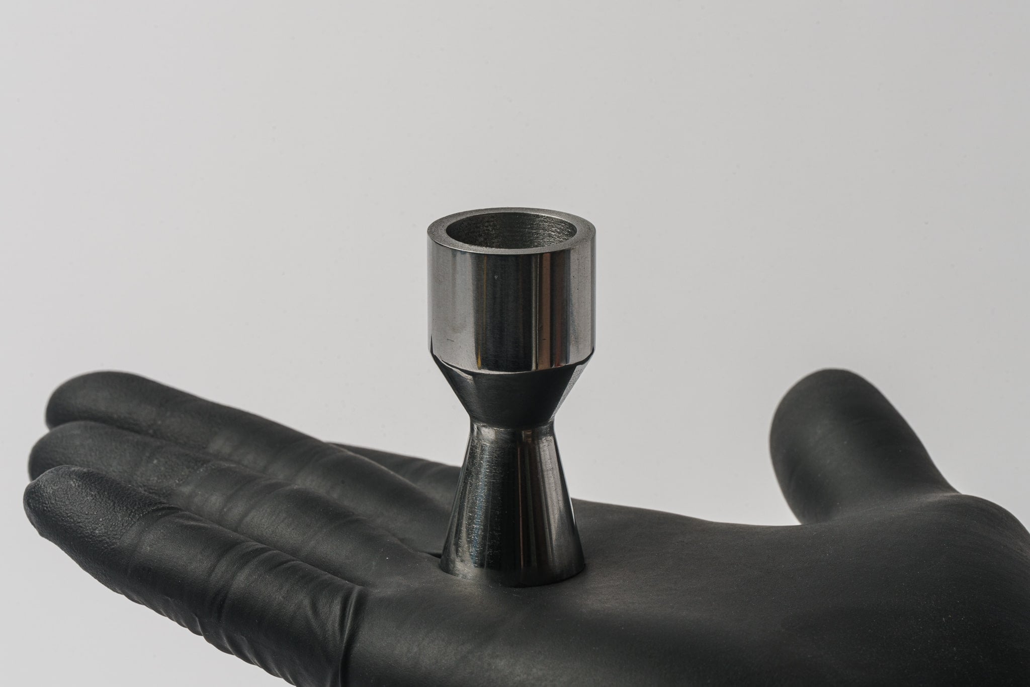 A gloved hand holds a metal part shaped like a rocket nozzle.