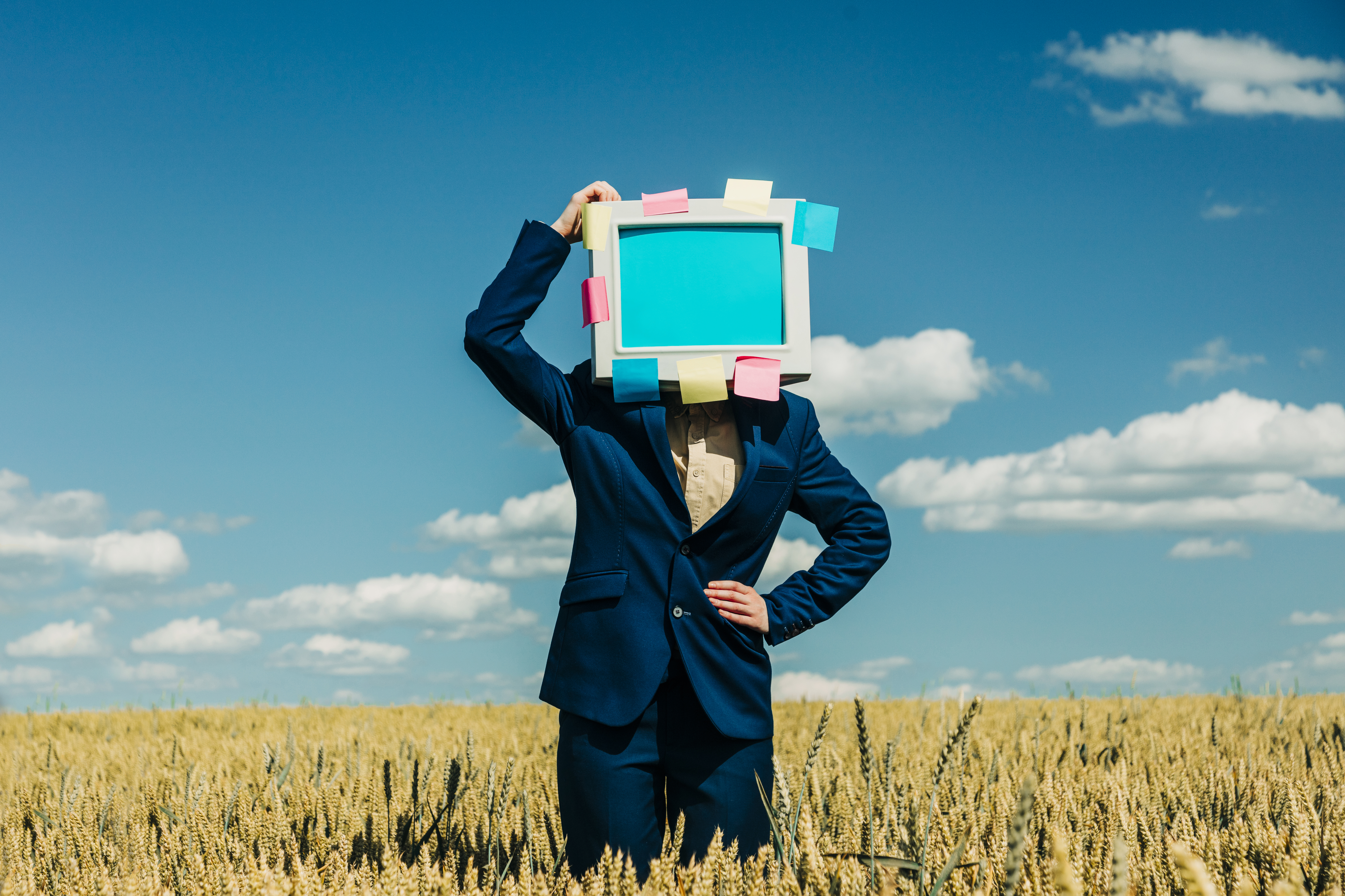 Businesswoman with retro monitor head standing in wheat field under blue sky