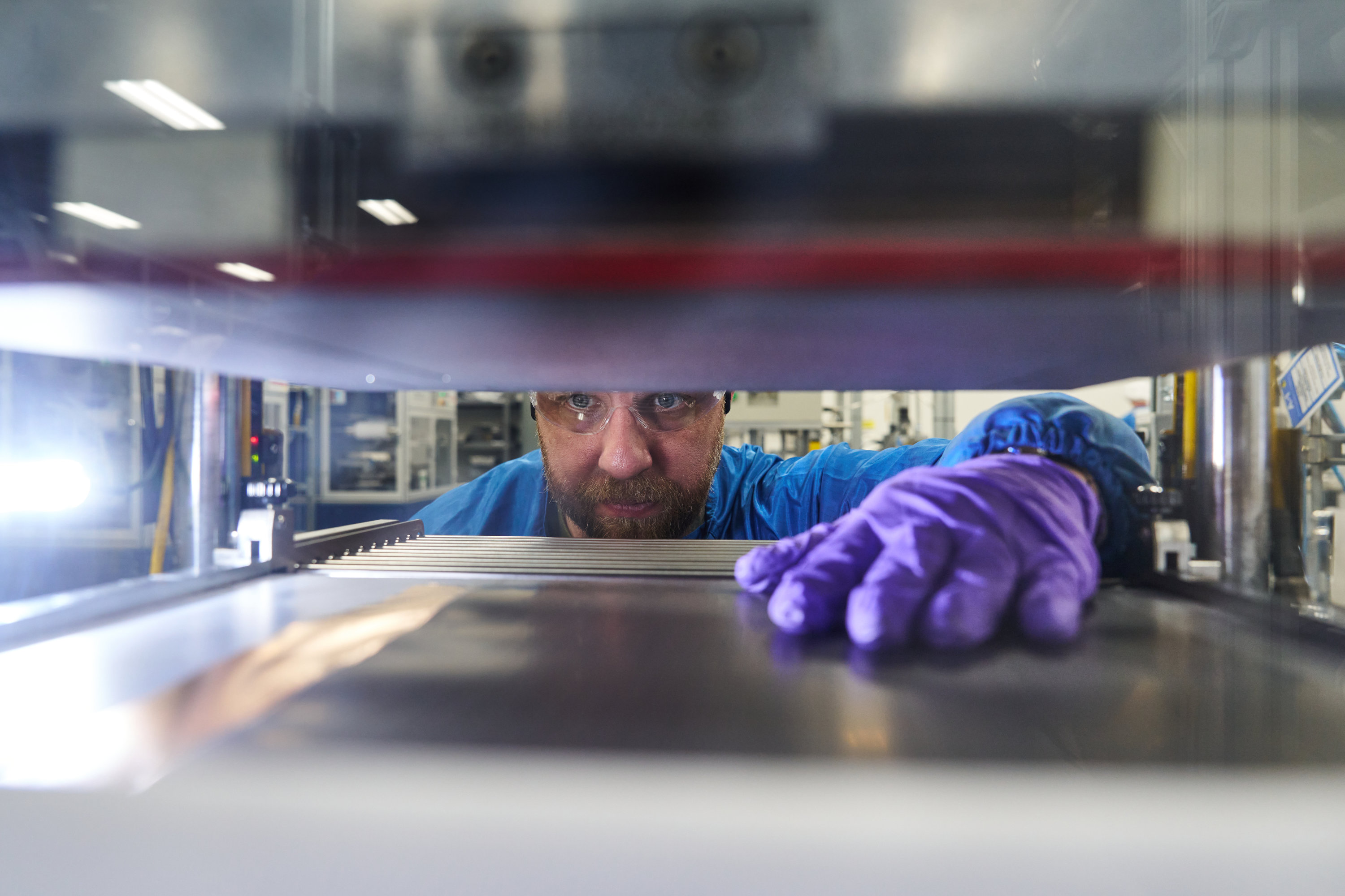 A man reaches his hand into a machine to grab a battery prototype.