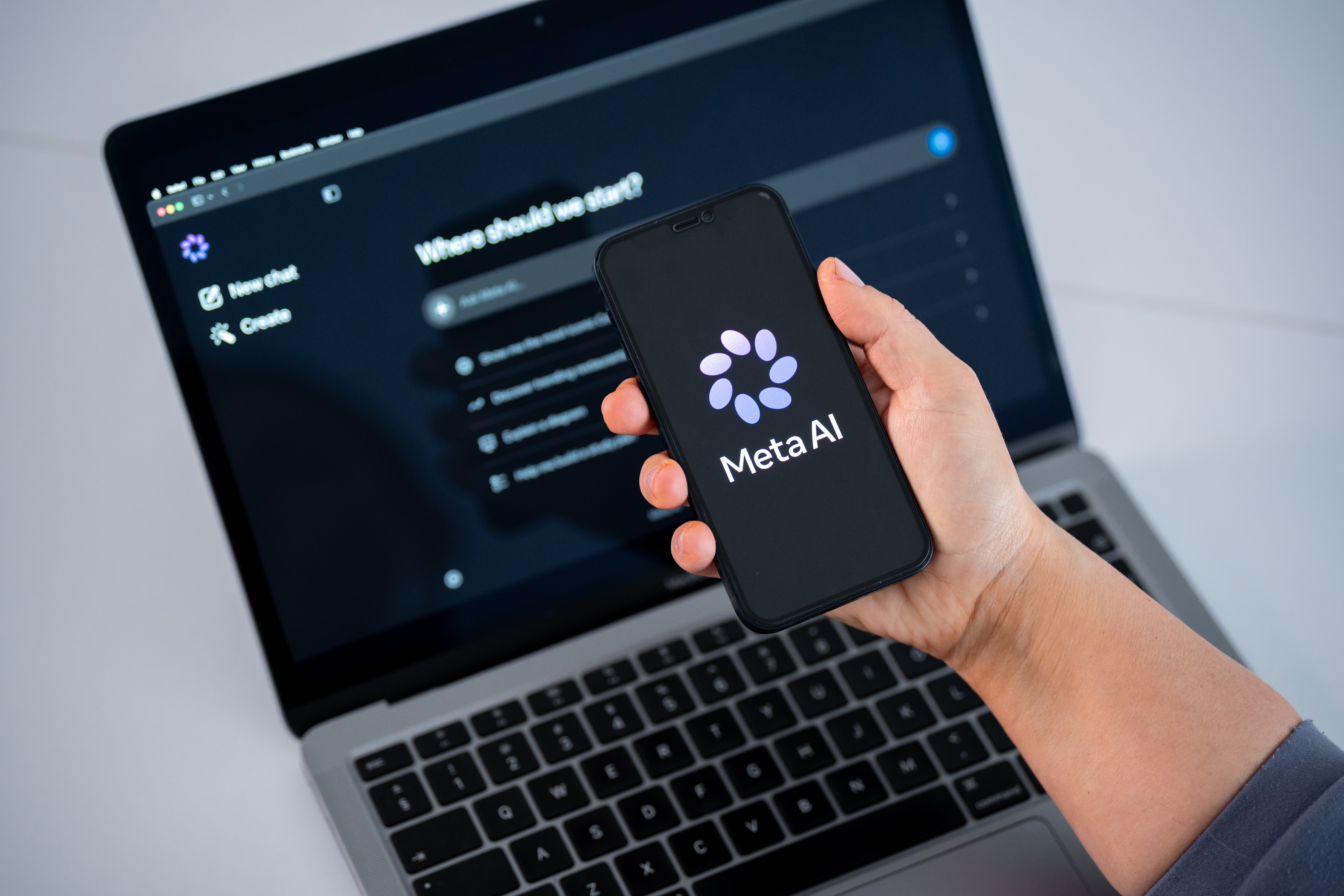 The Meta AI logo is seen on a smartphone screen, and a chatbot website is displayed on a computer screen.